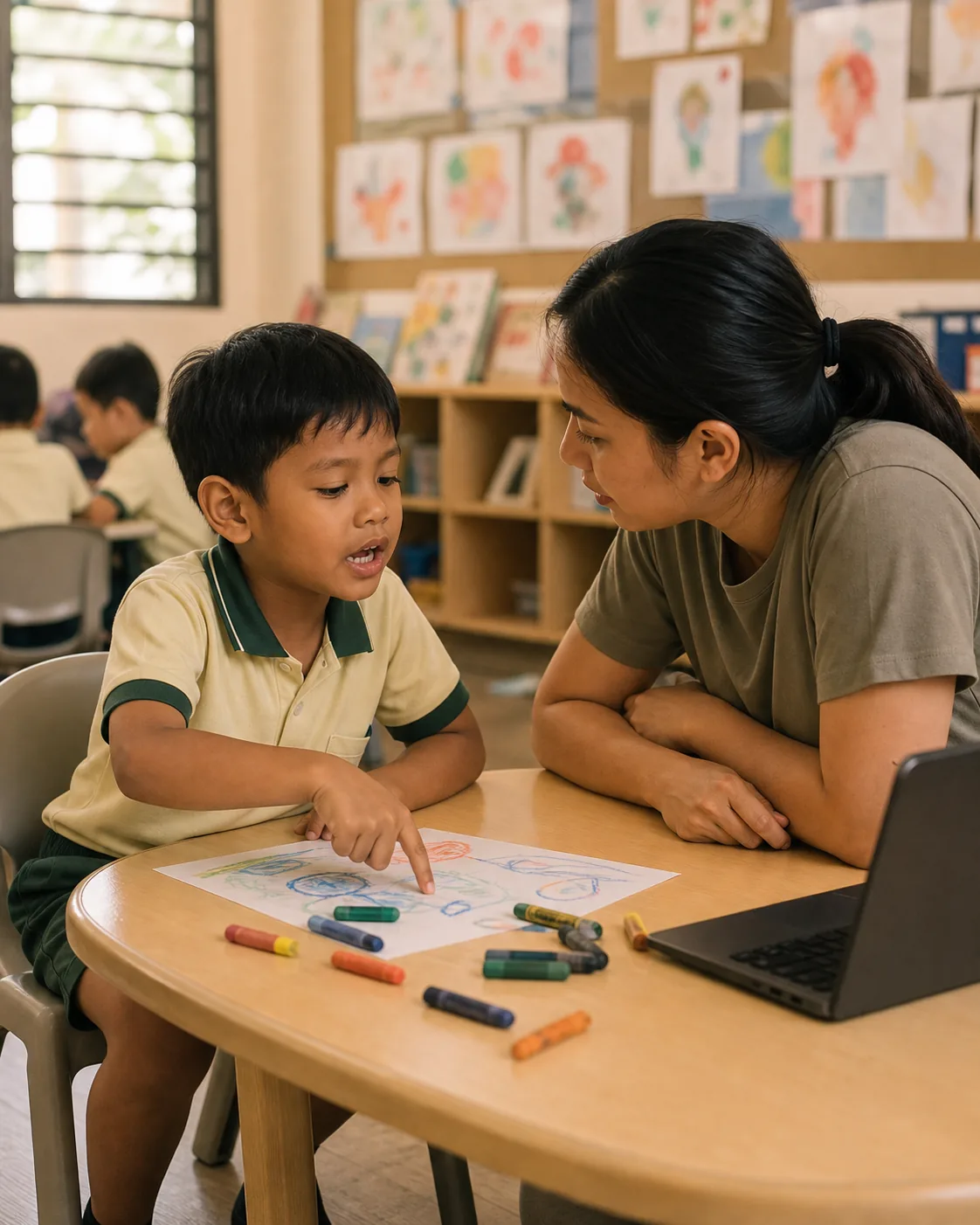 A child at a classroom table describing an idea while a workshop facilitator crouches beside them, listening.